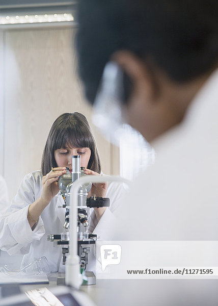 Female college student using microscope conducting scientific experiment in science laboratory classroom