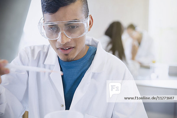 Male college student conducting scientific experiment in science laboratory classroom