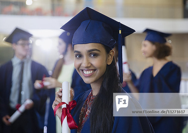 Portrait smiling female college student in cap and gown with diploma
