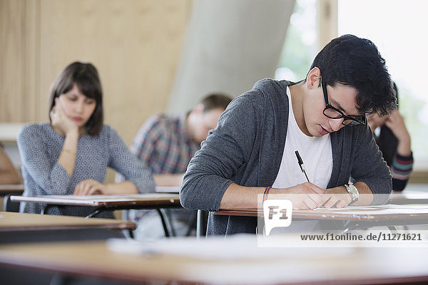 Focused male college student taking test at desk in classroom