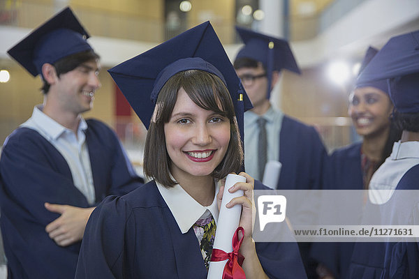 Portrait lächelnde Hochschulabsolventin in Mütze und Kleid mit Diplom