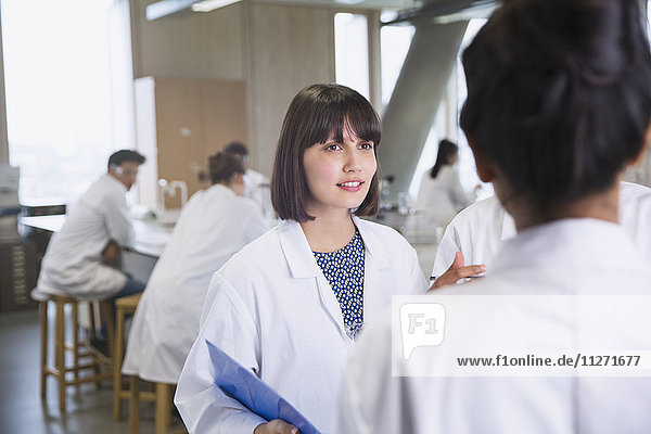 Female college students in lab coats talking in science laboratory classroom