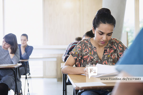 Serious female college student taking test at desk in classroom