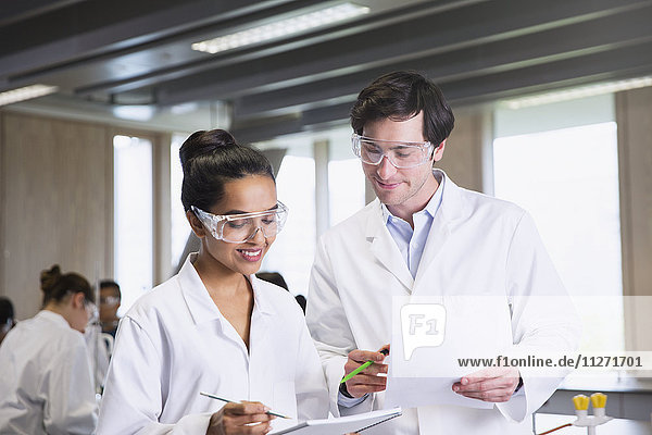 College students in lab coats discussing notes in science laboratory classroom