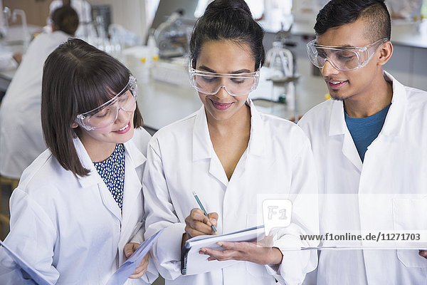 College students in lab coats discussing notes in science laboratory classroom