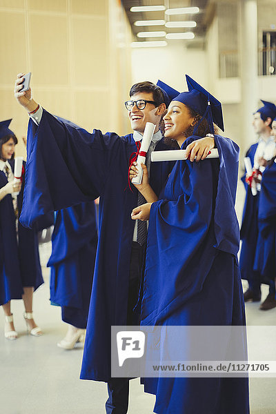 College graduates in cap and gown with diplomas taking selfie