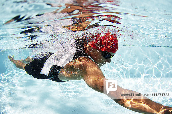 Männlicher Schwimmer  der im Schwimmbad unter Wasser schwimmt.