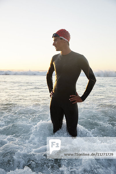 Male triathlete in wet suit standing in ocean surf