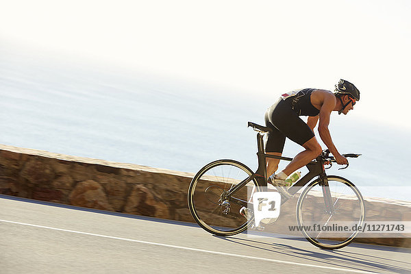 Male triathlete cyclist racing on ocean road