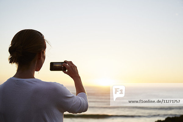 Woman photographing sunset over ocean with camera phone
