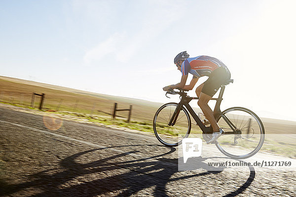 Male triathlete cyclist cycling on sunny rural road at sunrise