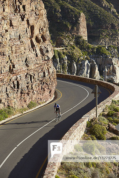 Male triathlete cyclist cycling uphill along sunny cliffs