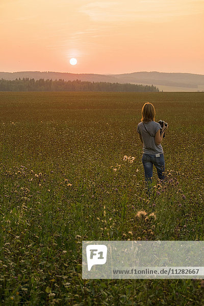Kaukasische Frau  die bei Sonnenuntergang mit einer Kamera durch ein Feld läuft