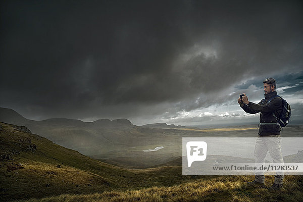 Caucasian hiker photographing storm clouds over landscape
