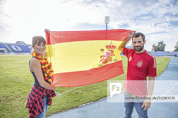 Young couple with face paint waving Spanish flag