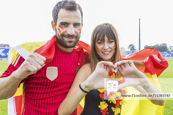 Junges Paar mit Gesichtsbemalung winkt mit spanischer Flagge