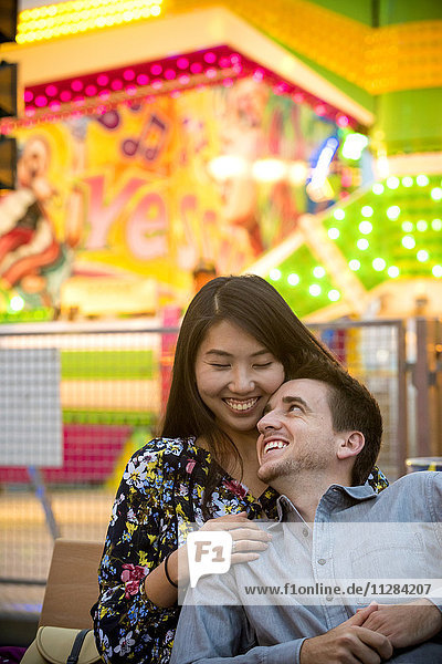 Smiling couple cuddling on bench in amusement park