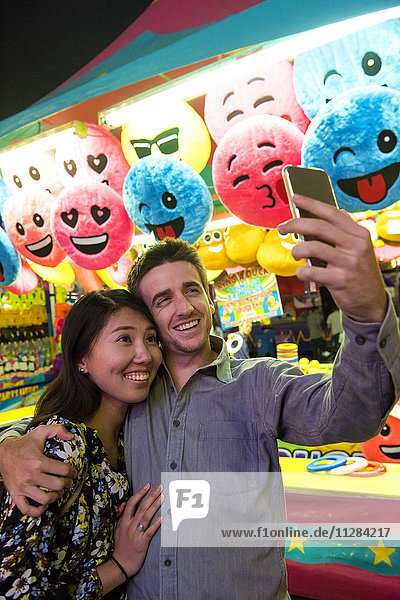 Lächelndes Paar posiert für Handy-Selfie im Vergnügungspark