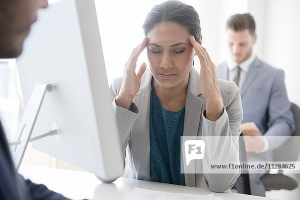 Geschäftsfrau mit Kopfschmerzen reibt sich im Büro die Schläfen