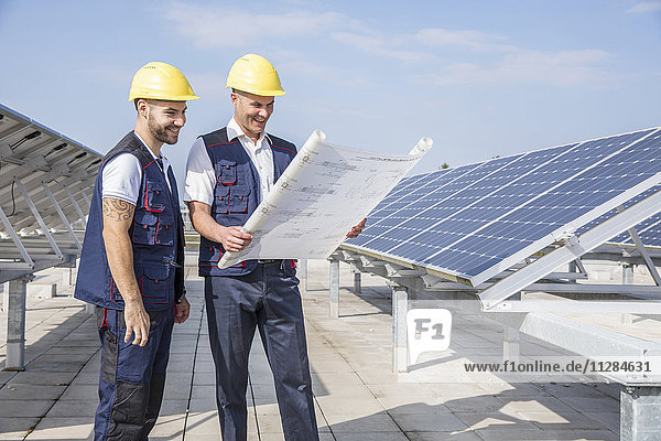 Bauarbeiter neben Sonnenkollektoren mit Blick auf den Bauplan