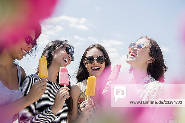 Lachende Frauen essen aromatisiertes Eis im Freien