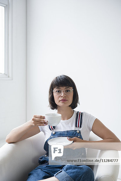 Porträt einer hispanischen Frau  die im Sessel Kaffee trinkt