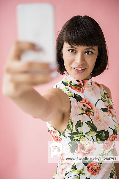 Hispanische Frau in geblümtem Kleid posiert für Handy-Selfie