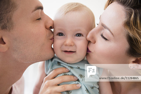 Caucasian mother and father kissing cheeks of baby son