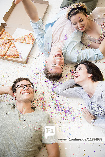 Caucasian friends laying on floor with pizza and confetti