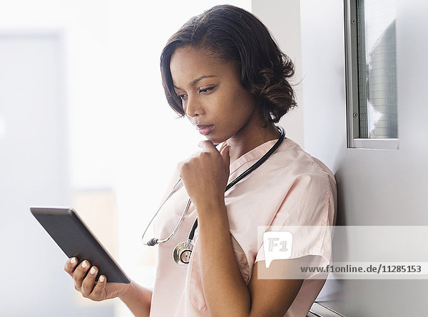 Gemischtrassige Krankenschwester mit digitaler Tafel an die Tür gelehnt