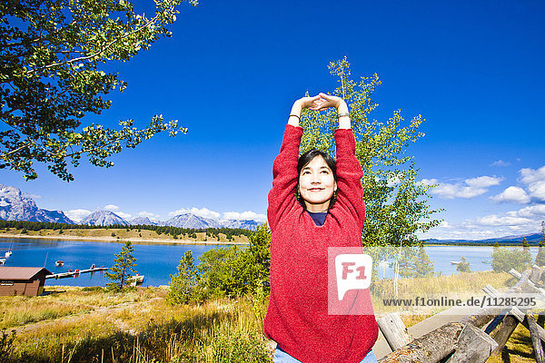 Lächelnde Japanerin  die ihre Arme in der Nähe eines Sees ausstreckt