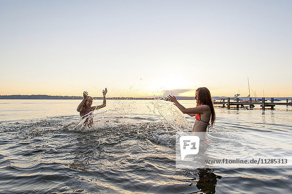 Two young women splashing each other in lake, Two young women splashing each other in lake