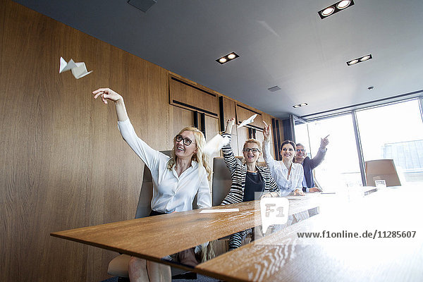 Business people in board room throwing paper airplanes