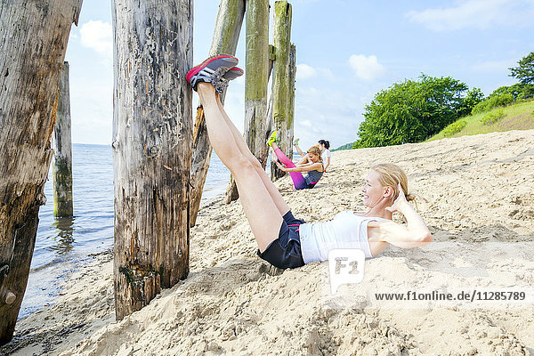 Young women on beach doing sit-ups