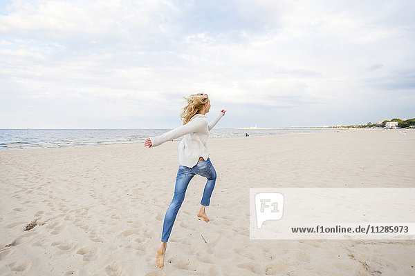 Frau mit blondem Haar läuft am Strand entlang