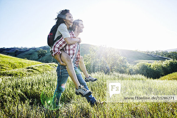 Smiling Man carrying girlfriend piggyback on hill