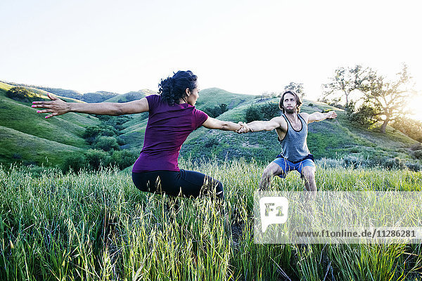 Couple holding hands and practicing yoga on hill
