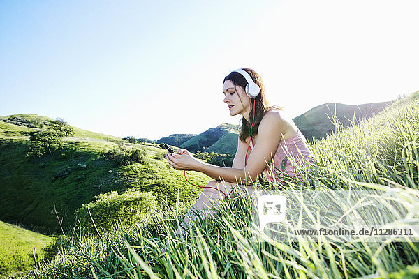 Kaukasische Frau sitzt auf einem Hügel und hört Kopfhörer