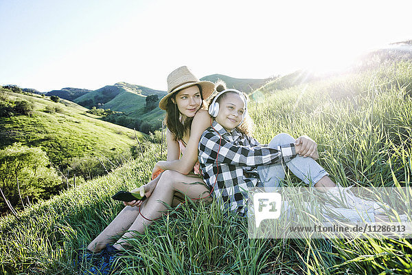 Mutter und Tochter sitzen auf einem Hügel und hören Kopfhörer