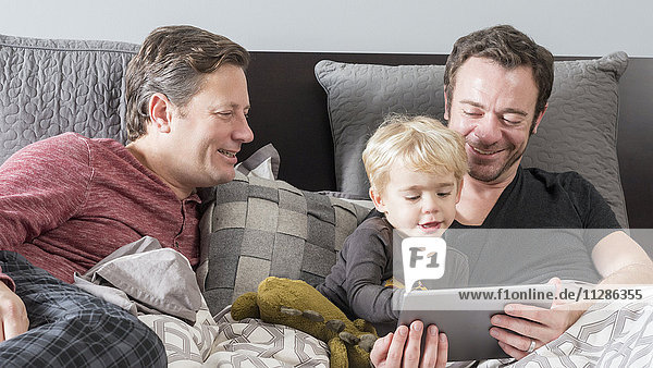 Caucasian fathers using digital tablet on bed with son