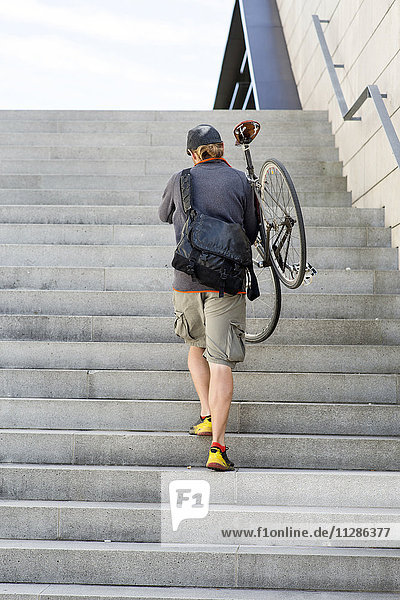 Bike messenger walking up stairway carrying bike