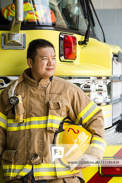 Chinesischer Feuerwehrmann in der Nähe von Feuerwehrautos stehend
