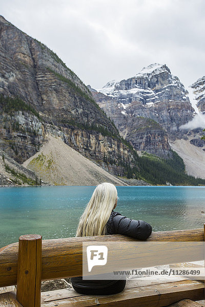 Weiße Frau sitzt auf einer Bank am Bergsee