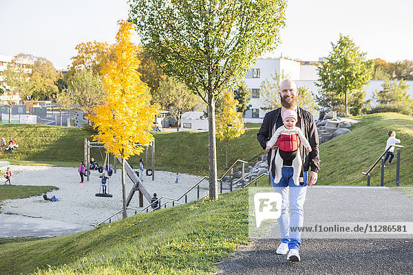 Father with baby girl in baby carrier walking in park