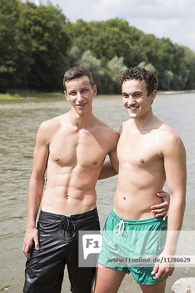 Two young shirtless men on the riverbank