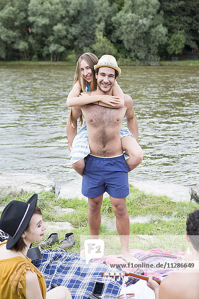 Junger Mann nimmt seine Freundin am Flussufer Huckepack