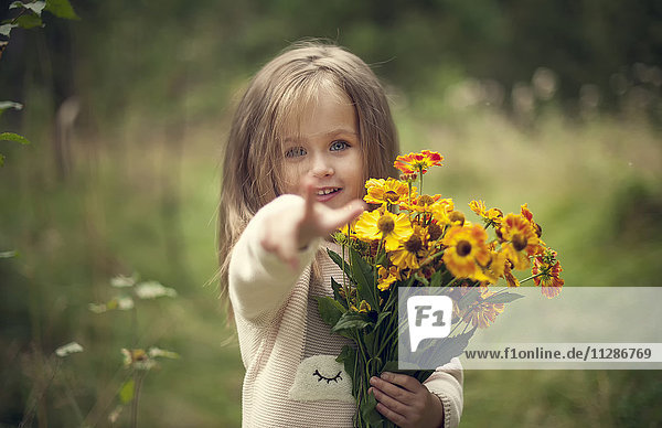 Lächelndes kaukasisches Mädchen zeigt mit dem Finger und hält Blumen