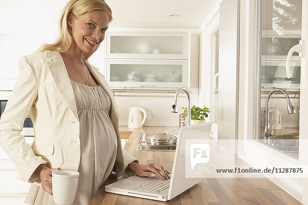 Schwangere Frau benutzt Laptop in der Küche
