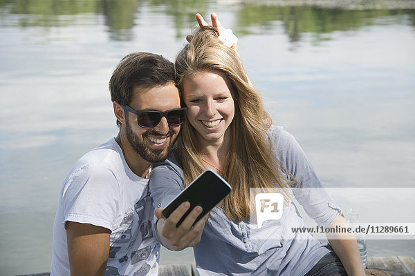 Verspieltes junges Paar am See mit einem Selfie