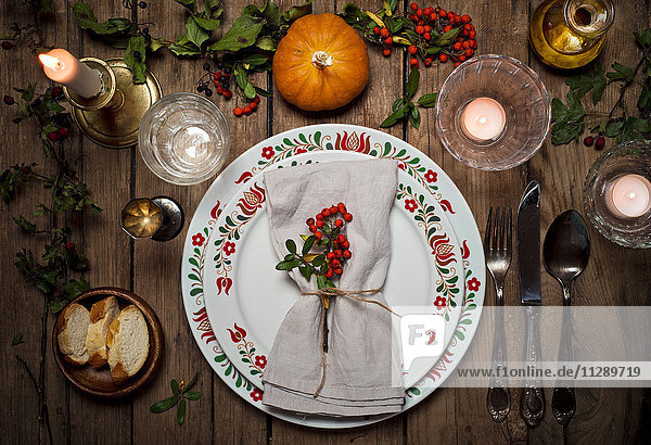Herbstlich gedeckter Tisch mit Kürbis  Stechpalme und Kerzenlicht